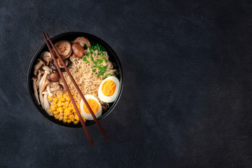 Ramen. Soba noodles with eggs, shiitake mushrooms, and vegetables, overhead shot on a dark background with chopsticks and a place for text
