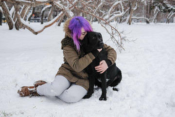 Fototapeta na wymiar A young woman plays with her pet black Labrador outside in winter.