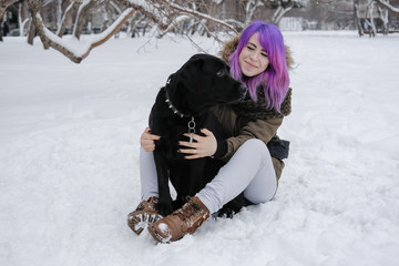 A young woman plays with her pet black Labrador outside in winter.