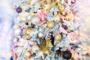 Obraz premium Close-up shiny pink gold decorated Christmas tree with lights ribbons, baubles and balls at house indoors. Xmas decoration background. Winter holidays card. Toned with bright bokeh lights