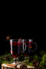 Two glasses with homemade mulled wine on a wooden saw. Black background. Real spruce branches. Fir cones.