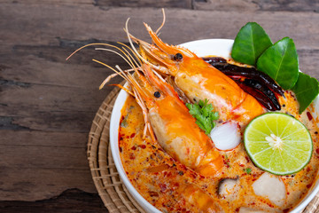 Tom Yum Goong or Shrimp soup spicy sour Soup Traditional food in Thailand contains chili, lime,lemongrass, lime leaf, along with cooked rice in a white dish on the old wood background from top view.