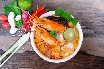 Tom Yum Goong or Shrimp soup spicy sour Soup Traditional food in Thailand contains chili, lime,lemongrass, lime leaf, along with cooked rice in a white dish on the old wood background from top view.