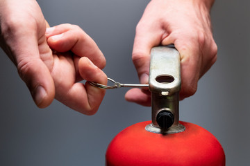 Actions in case of fire. Pull the safety pin out of the fire extinguisher by the ring. Men's hands close-up. Safety measures in the office and in the workplace. Emergency Prevention. Grey background.