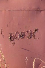 The inscription "bonus" in Russian made by welding on an uneven metal surface. Iron wall is dark red. Perfect for background and grunge design.