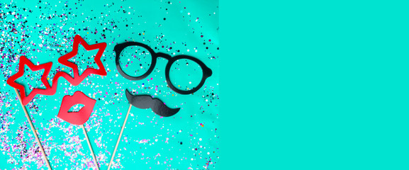 Festive composition with moustache, glasses, red mouth lips photo props and colorful confetti on green mint background/ Male and female concept, copy space