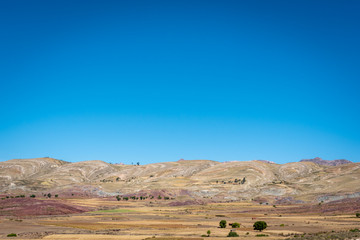 The inside of the Maragua Crater is filled with colourful ground and scattered trees on a clear and sunny day in Bolivia.