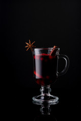 A glass of homemade cranberry-apple mulled wine on a black glossy background. Cinnamon stick. Anise star. Isolate.