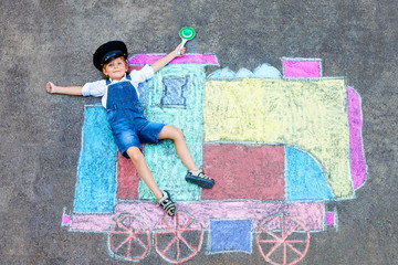 Happy little kid boy having fun with train or steam locomotive picture drawing with colorful chalks...