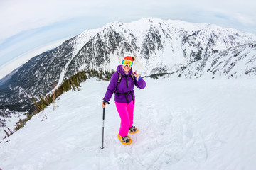 Woman hikeing in the snowy mountains with a phone and snowshoes. and backpack