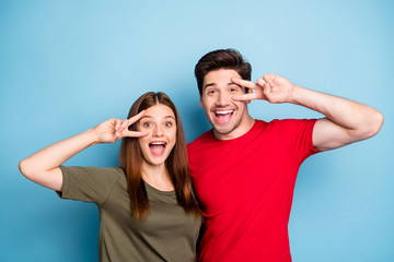 Portrait of funky two people spouses students fun on summer weekends relax rest make v-signs near face wear casual style outfit isolated over blue color background