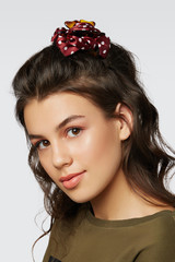 Closeup half-turn face portrait of girl with dark wavy hair, wearing khaki t-shirt. Her hair is pulling with brown hairpin crab with red polka dot bow. Girl is looking straight and smiling.