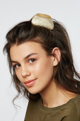 Closeup half-turn face portrait of girl with dark wavy hair, wearing khaki t-shirt. Her hair is...
