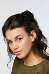 Closeup half-turn face portrait of girl with dark wavy hair, wearing khaki t-shirt. Her hair is pulling with black round hairpin crab with black mother-of-pearl insert. Girl is looking straight and sm