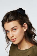 Closeup half-turn face portrait of girl with dark wavy hair, wearing khaki t-shirt. Her hair is...