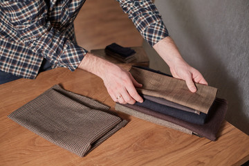 Tailor Selects wool from the stack. Young man working as a tailor and using a sewing machine in workshop.