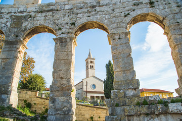 Ancient heritage in Pula, Istria, Croatia. Catholic church tower bell, view through the arches of monumental ancient Roman arena. Interior of historic amphitheater, wide angle view of high walls on bl