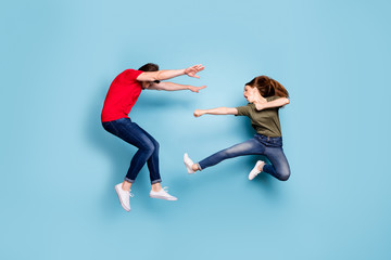 Fototapeta na wymiar Full length photo of crazy mad two people spouses woman disagree jump fight kick man fall wear green red t-shirt denim jeans sneakers isolated over blue color background