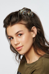 Closeup half-turn face portrait of girl with dark wavy hair, wearing khaki t-shirt. Her hair is...