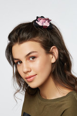 Closeup half-turn face portrait of girl with dark wavy hair, wearing khaki t-shirt. Her hair is pulling with black hairpin crab with pastel pink lilium flower painting. 