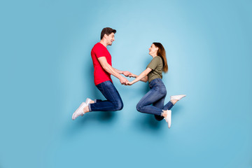 Full body profile side photo of charming two spouses relax rest on spring holidays jump hold hands feel content wear casual style clothes isolated over blue color background
