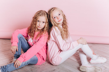 Obraz na płótnie Canvas Close up portrait of young cute adorable caucasian sisters with curly hairstyle on soft pink background indoors in studio. Positive leisure concept, childhood happiness concept.