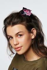 Closeup half-turn face portrait of girl with dark wavy hair, wearing khaki t-shirt. Her hair is pulling with black hairpin crab with crimson peony flower painting. Girl is looking straight and smiling