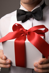 Portrait of an unrecognizable man in formal black tie tuxedo holding a gift with a silken red bow