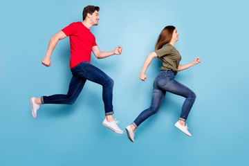 Fototapeta na wymiar Full body profile side photo of cheerful excited couple jump run hurry for summer sales wear green red t-shirt denim jeans sneakers isolated over blue color background