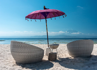 two resort chairs and a purple umbrella on a beach in bali at low tide