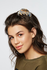 Closeup half-turn face portrait of girl with dark wavy hair, wearing khaki t-shirt. Her hair is pulling with multi-colored mother-of-pearl hairpin crab. Girl is looking straight and smiling. 