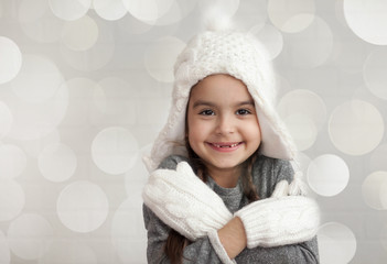 Happy laughing child girl in a winter white knitted hat and mittens on light background
