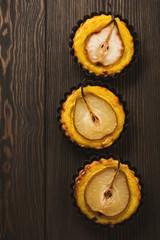 Pears and custard mini tarts on a dark brown wooden old table background. Top view.