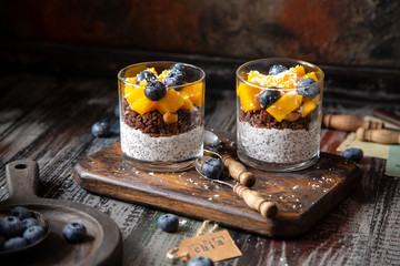 healthy layered dessert white chia seeds pudding, chocolate granola, mango, blueberries