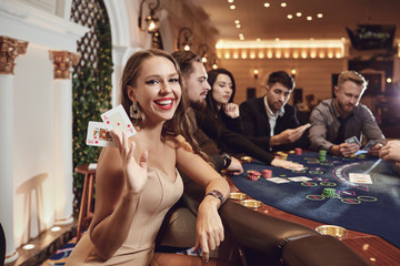Girl with cards in her hands smiling plays poker in a casino. - obrazy, fototapety, plakaty
