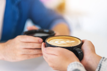 Closeup image of a man and a woman holding two coffee cups together