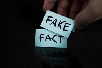 The fact is replaced by a fake. substitution of concepts. a man changes the signs with the words fact on fake on a black background. - obrazy, fototapety, plakaty
