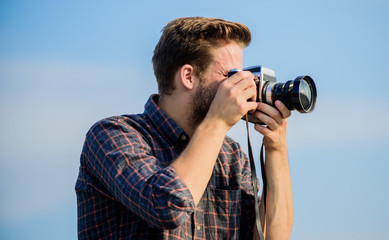 Guy outdoors blue sky background. Handsome blogger guy traveler retro camera. Reporter taking...