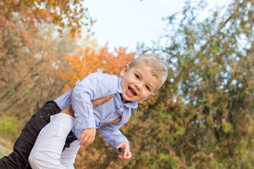 little blond boy in autumn forest plays with autumn foliage