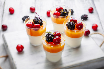 4 cups mango pannacota on wooden tray with blackberries and cherries