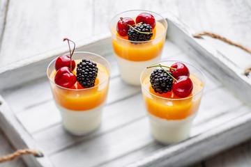 3 cups mango pannacota on wooden tray with blackberries and cherries