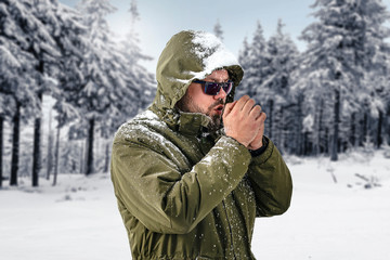 Fototapeta na wymiar Hipster in green jacket walks through the forest.Man with a beard at the age of 25.Winter Christmas time. Landscape of fir trees covered with snow and frost.Copy space.Snowflakes and cold day.