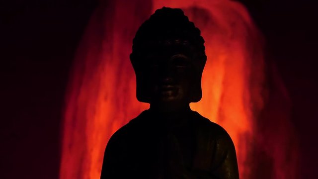 buddha statue illuminated by the faint light of a candle with incense plume and swinging light