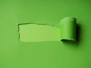 Small paper hole with torn sides over green background for your text, print or promotional content. Through paper. Ripped hole. No people. Accurate shot. Advertising and breakthrough concept