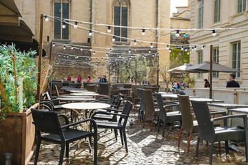  Documentary image. Avignon. Provence. France. October 25. 2019. Restaurant  empty tables in Avignon's Old Town Square. It is sunny and raining at the same time. Garlands of light bulbs over tables.