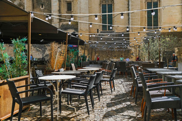  Documentary image. Avignon. Provence. France. October 25. 2019. Restaurant empty tables in Avignon's Old Town Square. It is sunny and raining at the same time. Garlands of light bulbs over tables. 