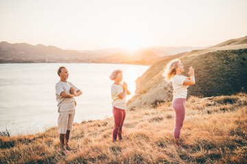 Group of senior people doing yoga exercises at the mountain on the background at the sunset....