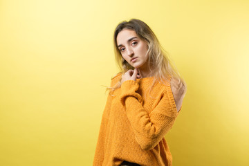 Portrait of a beautiful girl in an orange sweater, looks aside with pensive expression, is considering a plan for further action.