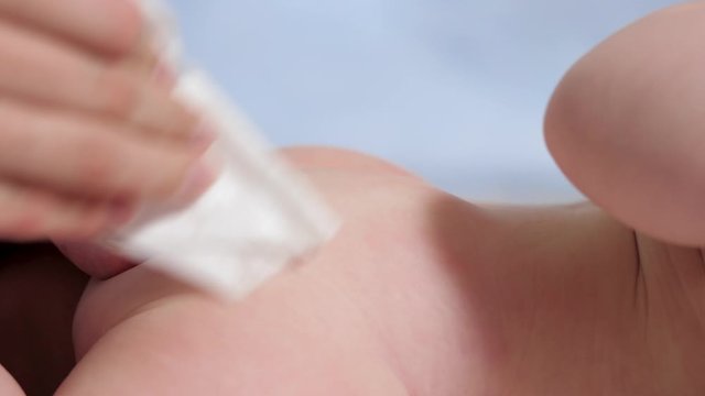 Mom wipes baby's buttocks with wet wipe. Child lies on white blanket on blue background, mother wipes his buttocks with wet cloth. Slow motion