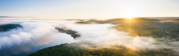 Fog over lake and taiga forest at sunrise, aerial view wide panorama. Nature landscape in Ural, Russia
